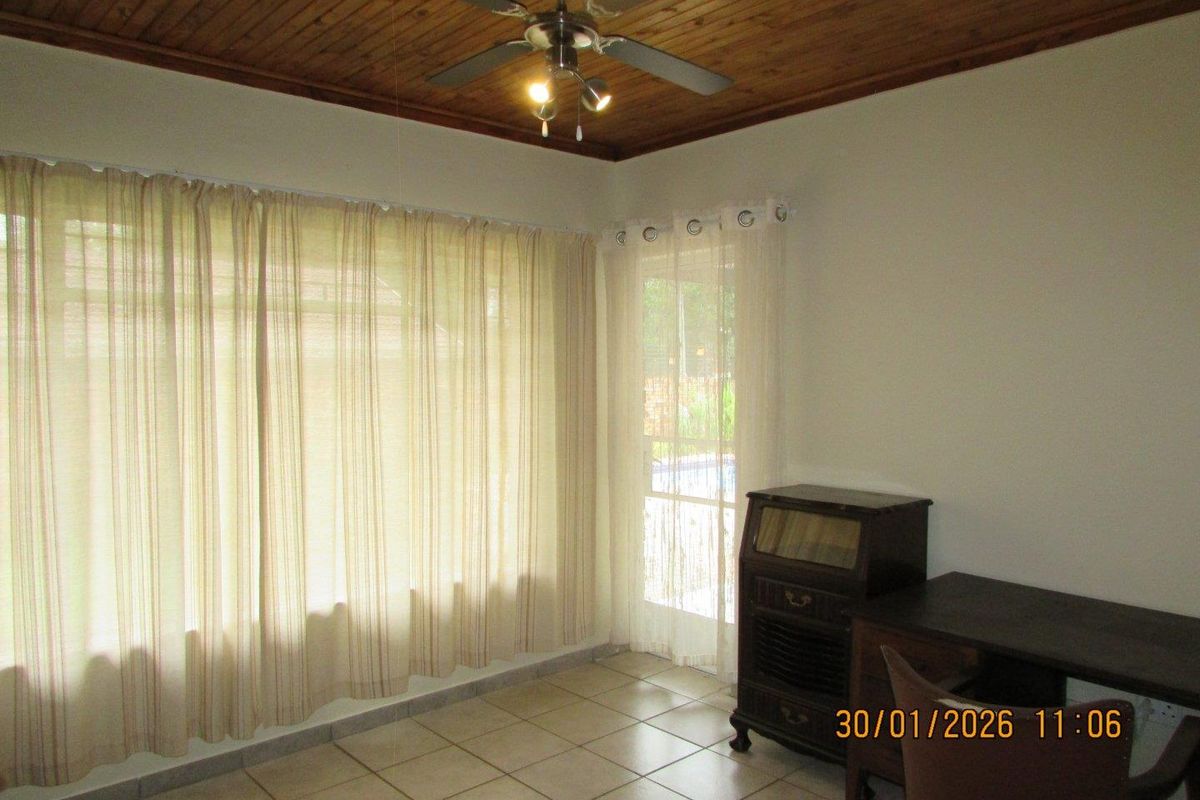 A living area featuring tiled flooring, a timber-paneled ceiling with a central fan, and direct access to the outdoor area through a glass door.