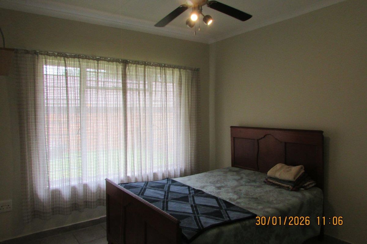 A standard bedroom featuring tiled flooring, a ceiling fan, and a large window with curtains.