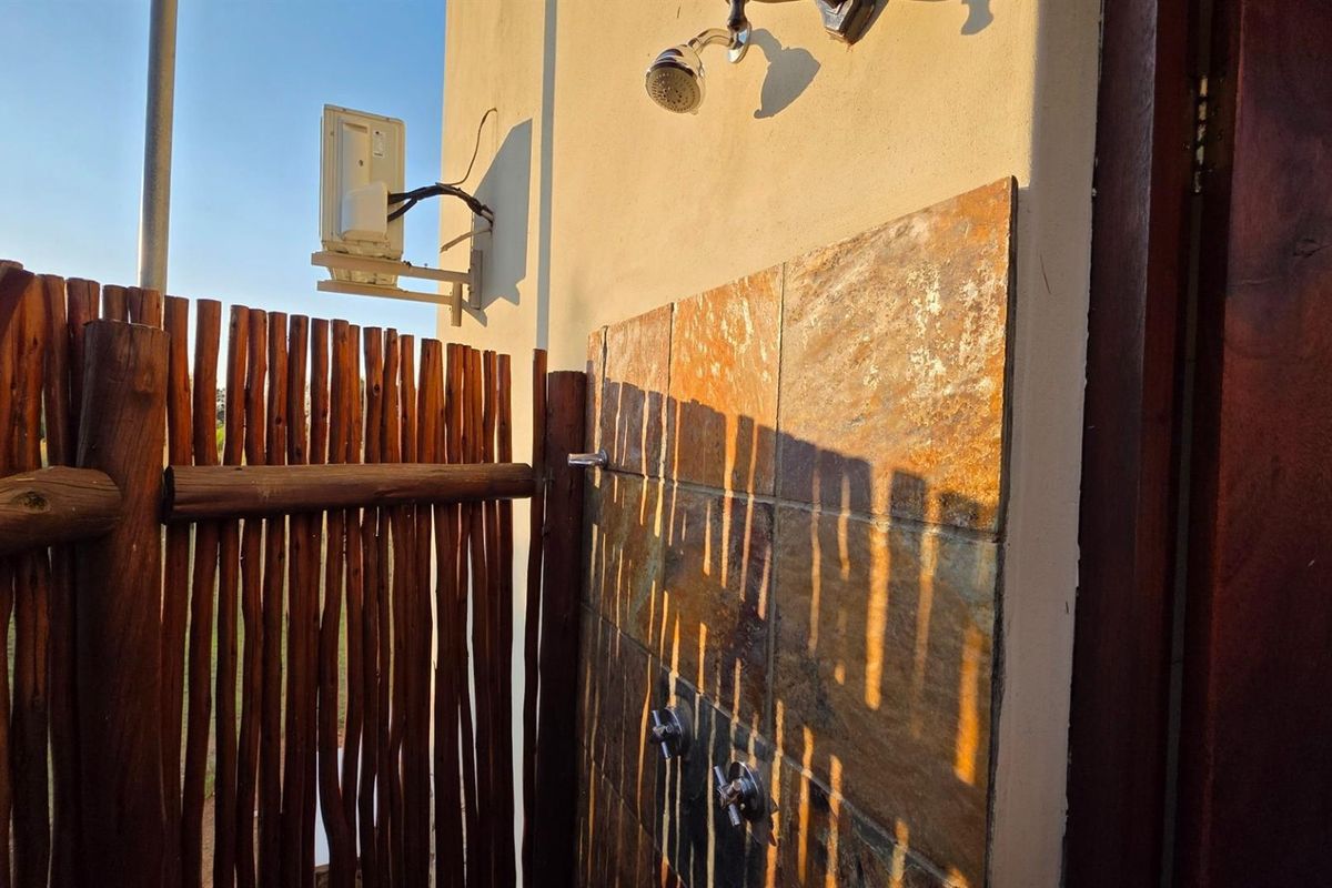 An outdoor shower area featuring stone tile wall cladding and rustic timber pole fencing, providing a private and functional exterior wash space.