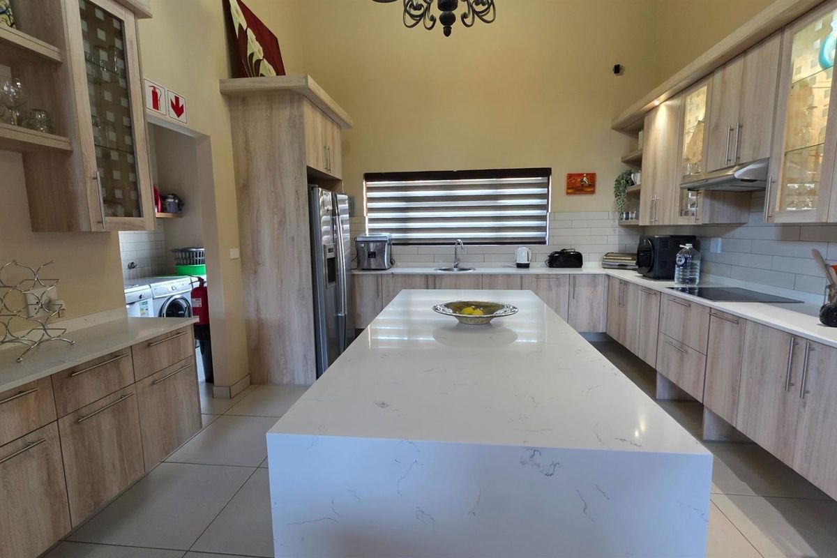 Spacious modern kitchen featuring a large central island with quartz countertops, ample built-in cabinetry, and integrated appliances, complemented by neutral tiled flooring.