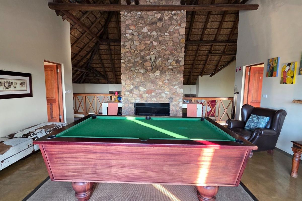 Spacious living area featuring a prominent stone fireplace, high vaulted thatched ceiling with exposed timber rafters, and polished concrete flooring.