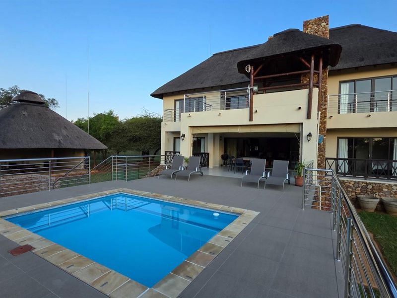Spacious outdoor pool area featuring a tiled deck, stainless steel balustrades, and a multi-level residence with a traditional thatched roof.