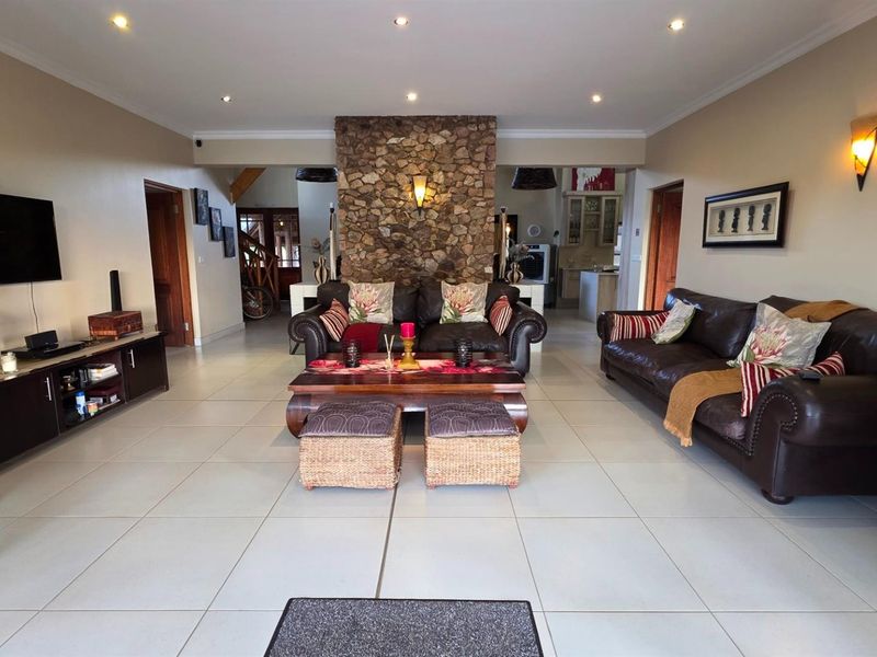 Spacious open-plan living area featuring a prominent stone fireplace, neutral tiled flooring, and recessed lighting, creating a warm and inviting atmosphere.