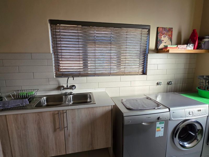 Functional laundry room featuring a double stainless steel sink, subway tile backsplash, and dedicated plumbing connections for laundry appliances.