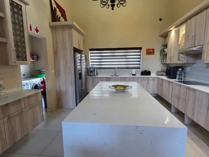 Spacious modern kitchen featuring a large central island with quartz countertops, ample built-in cabinetry, and integrated appliances, complemented by neutral tiled flooring.