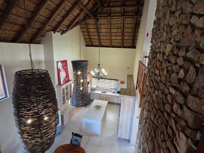 Spacious open-plan kitchen area featuring a high thatched ceiling with exposed timber trusses, a large stone feature wall, and modern cabinetry.