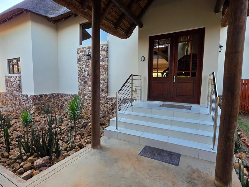 Front entrance featuring a thatched roof, stone cladding, timber support posts, and tiled steps with stainless steel handrails leading to double timber doors.