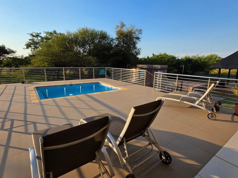 An elevated outdoor patio area featuring a swimming pool and modern stainless steel balustrades, overlooking a natural landscape.
