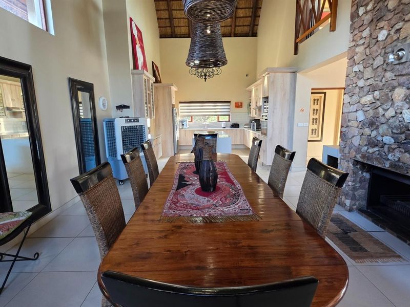 Spacious open-plan living and dining area featuring a prominent stone fireplace, high thatch ceilings, and an integrated kitchen with modern cabinetry.
