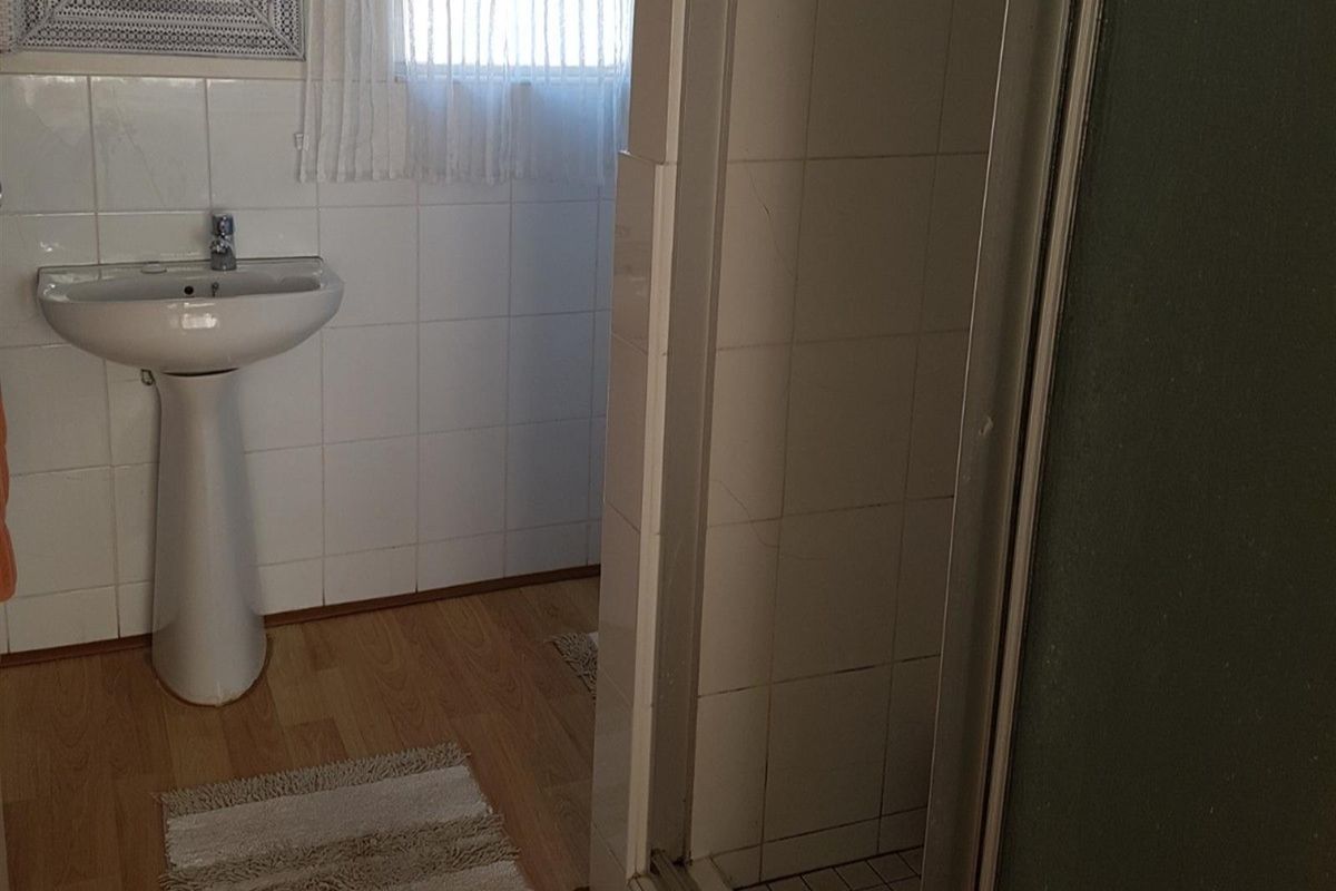 A functional bathroom featuring a pedestal basin, tiled walls, and a shower enclosure with a glass door.