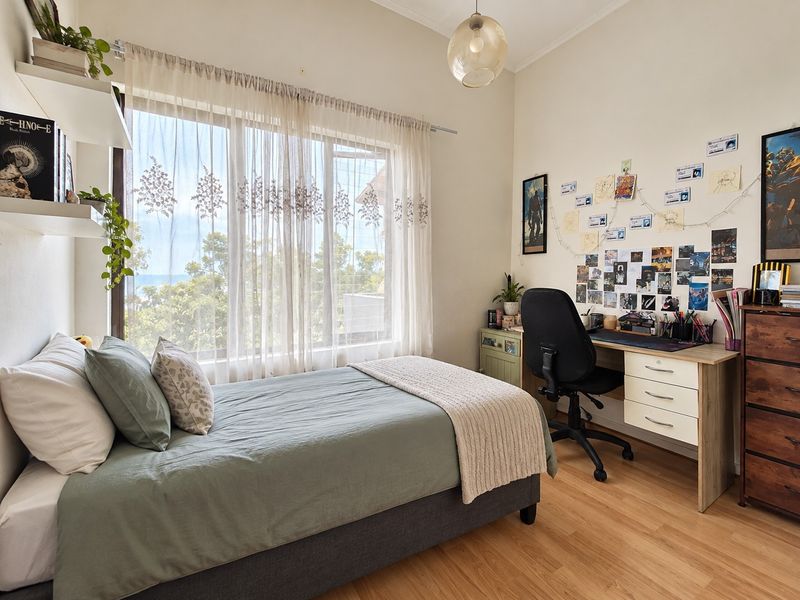 A bright and functional bedroom featuring laminate flooring, a large window with natural light, and built-in floating wall shelves.
