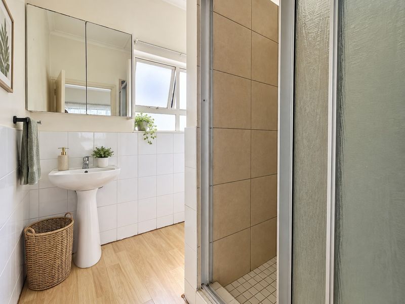 A functional bathroom featuring a pedestal sink, mirrored medicine cabinet, and a tiled shower enclosure with a neutral color palette.