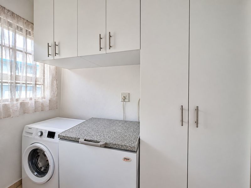 A functional laundry area featuring white built-in cabinetry, a laminate countertop, and space for laundry appliances.