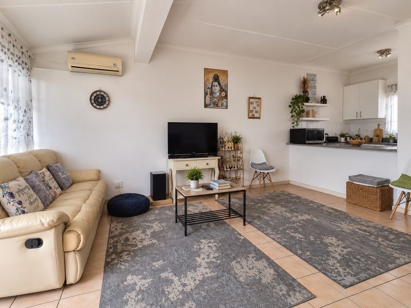 An open-plan living and kitchen area featuring tiled flooring, a wall-mounted air conditioner, and functional kitchen cabinetry with a breakfast counter.