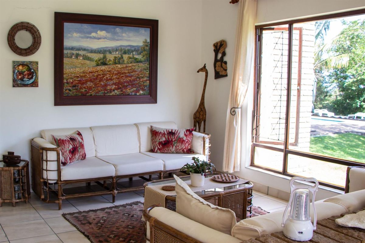 A bright living room featuring tiled flooring and large windows that provide natural light and a view of the outdoor garden area.