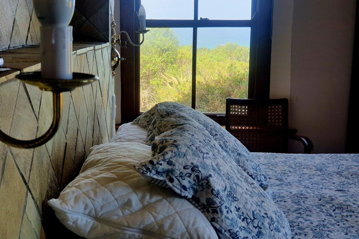A bedroom featuring a window with a scenic garden and coastal view, complemented by decorative wall tiling and wall-mounted light fixtures.