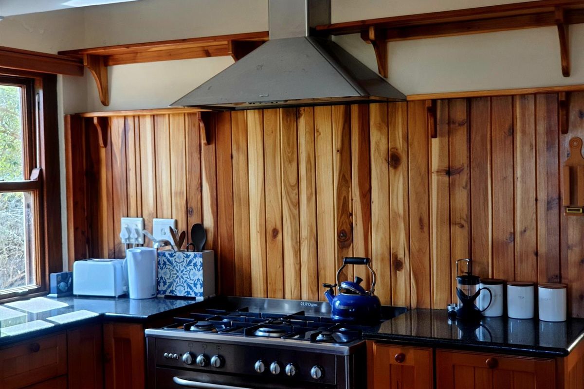 A kitchen featuring timber wall paneling, granite countertops, and a stainless steel gas stove with a matching extractor fan.