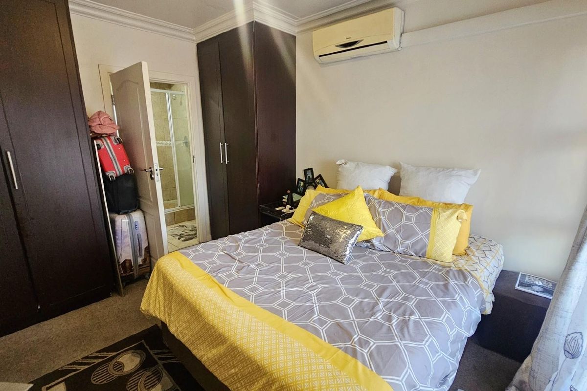 A bedroom featuring built-in dark wood cabinetry, an en-suite bathroom, and a wall-mounted air conditioning unit.