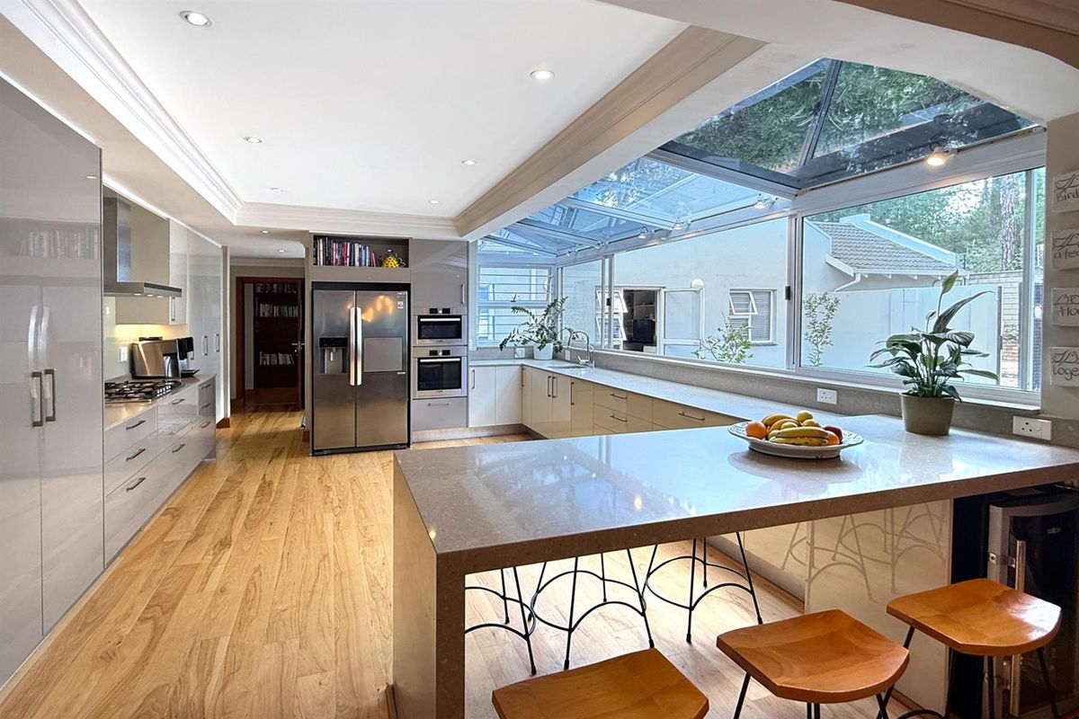 Modern kitchen featuring high-gloss cabinetry, stone countertops, a central island, built-in ovens, and a large glass skylight providing abundant natural light.