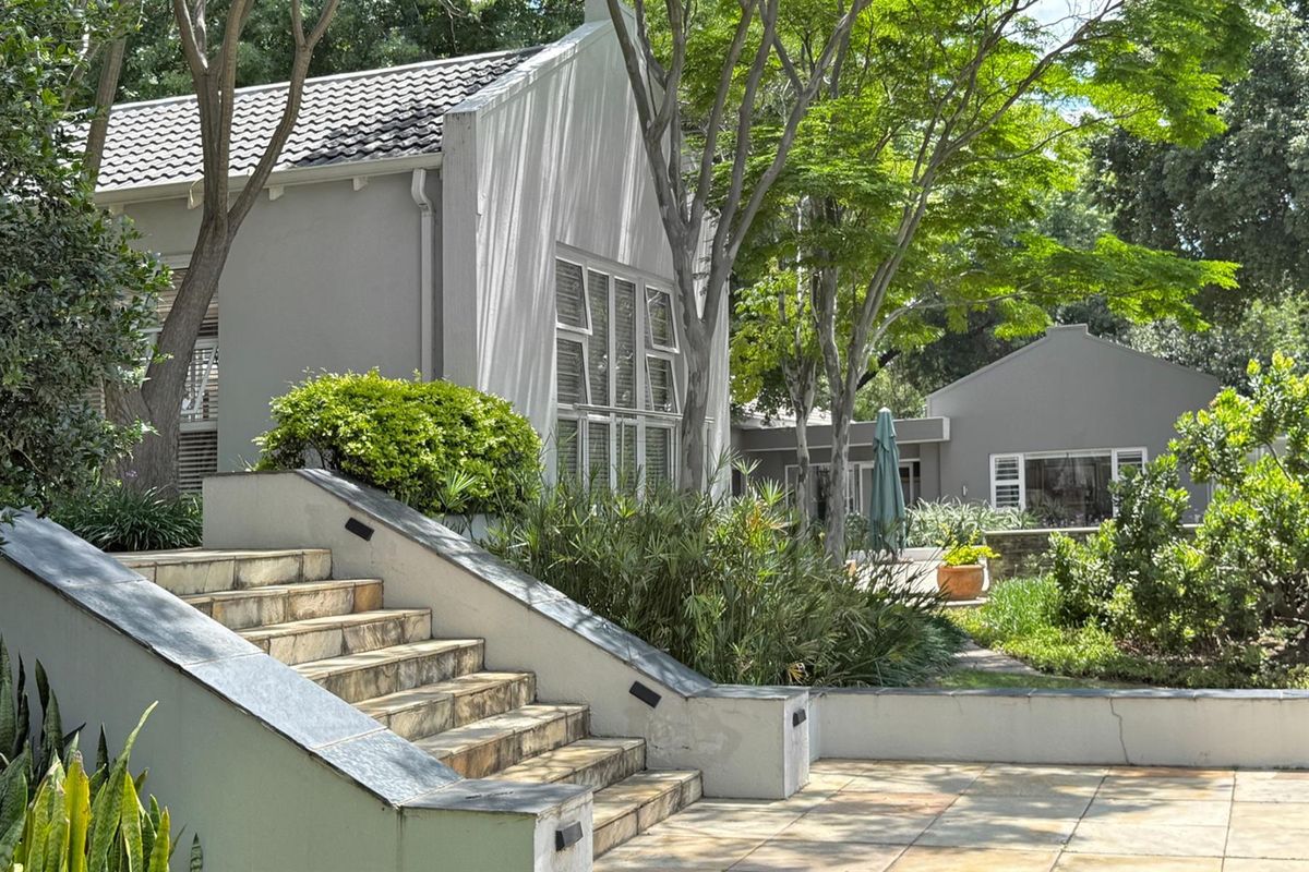 A well-maintained exterior view featuring stone-tiled stairs, landscaped garden areas, and a classic gabled roof design with neutral grey exterior walls.