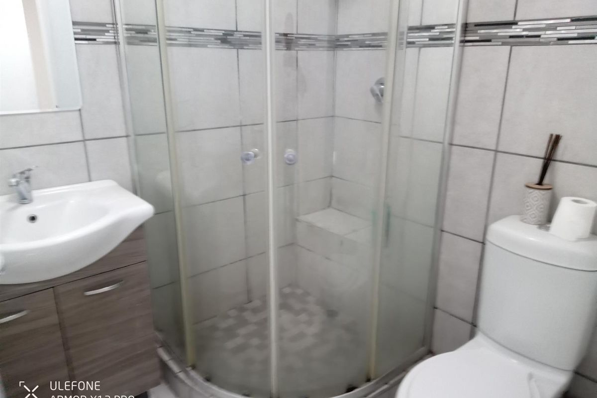 A functional bathroom featuring a corner shower enclosure, vanity cabinet with basin, and a standard toilet with tiled finishes.