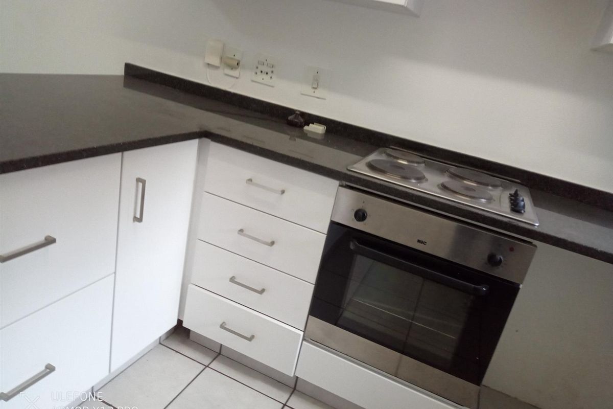 A clean, functional kitchen featuring white cabinetry, dark granite countertops, and a built-in oven with an electric hob.