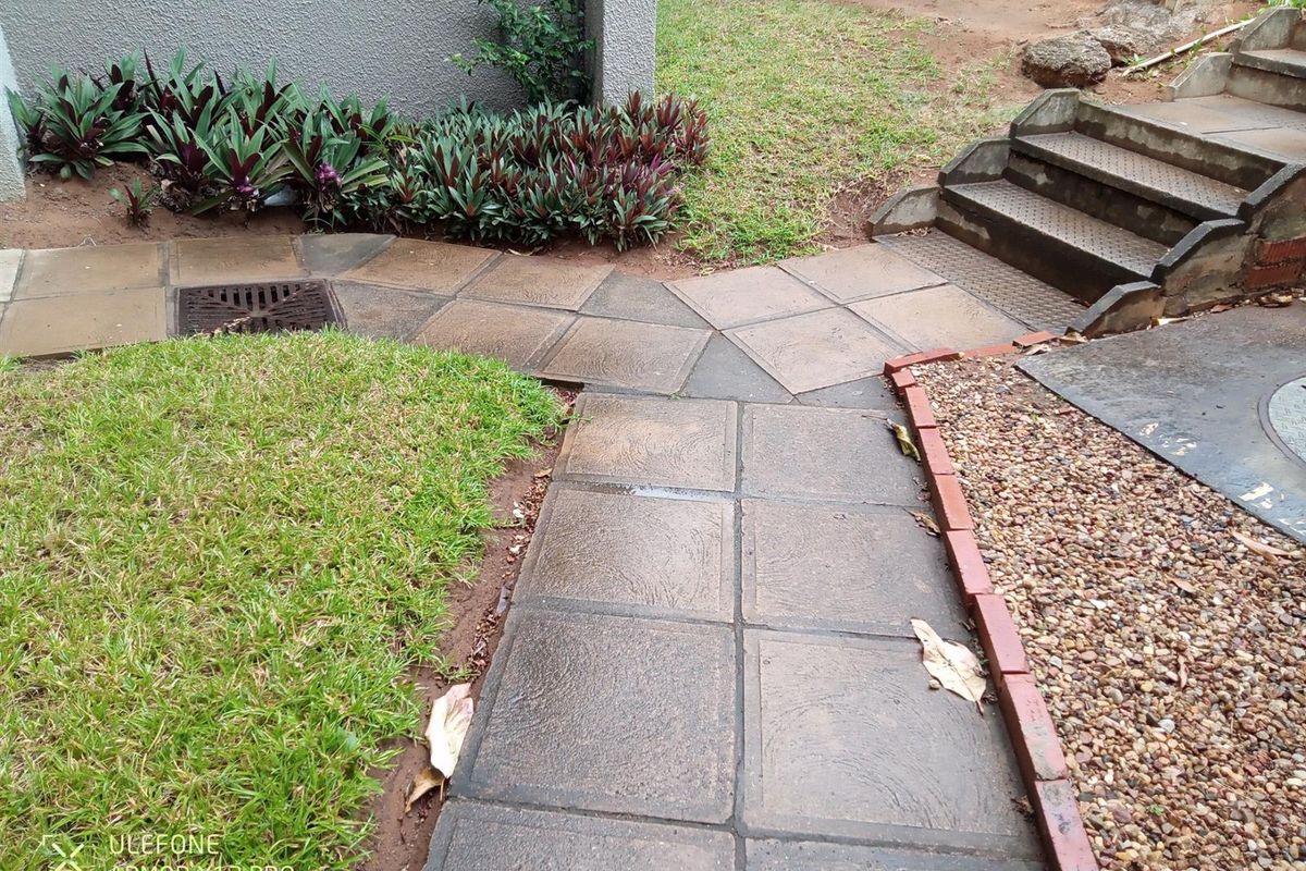 A paved garden walkway leading to concrete stairs, featuring brick edging, gravel landscaping, and a built-in stormwater drain.
