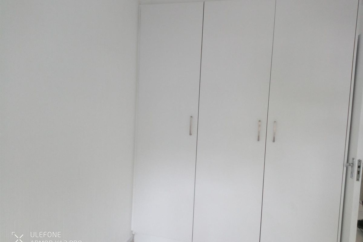 A clean, empty bedroom featuring white built-in cupboards with modern handles.