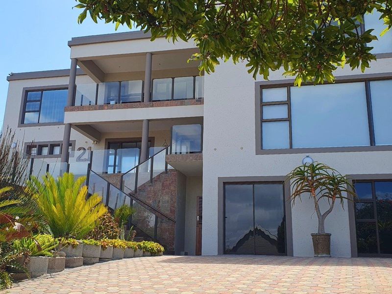 Modern multi-level residential facade featuring stone accents, glass balustrades, and a paved driveway entrance.