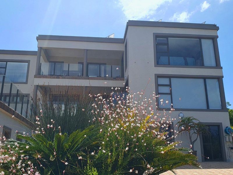 A modern multi-story residential exterior featuring large aluminium-framed windows, a spacious covered balcony with glass balustrades, and a paved approach.