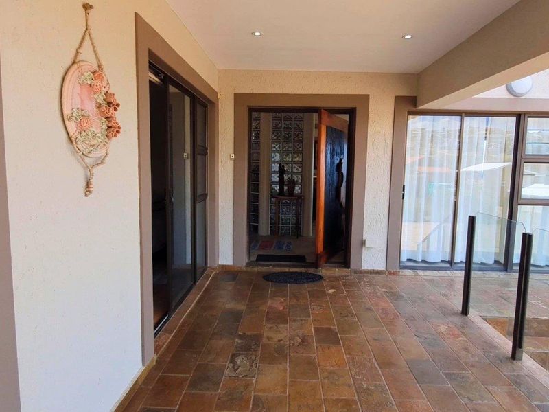 A covered patio area featuring tiled flooring, recessed lighting, and glass sliding doors leading into the home, complemented by a modern glass balustrade.