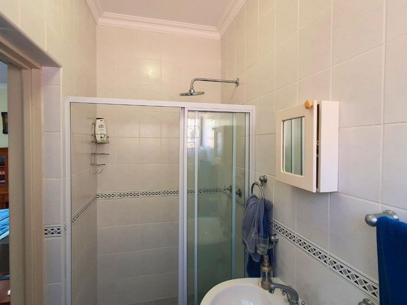 A functional bathroom featuring a tiled shower enclosure, pedestal basin, and wall-mounted medicine cabinet, with neutral wall tiling throughout.