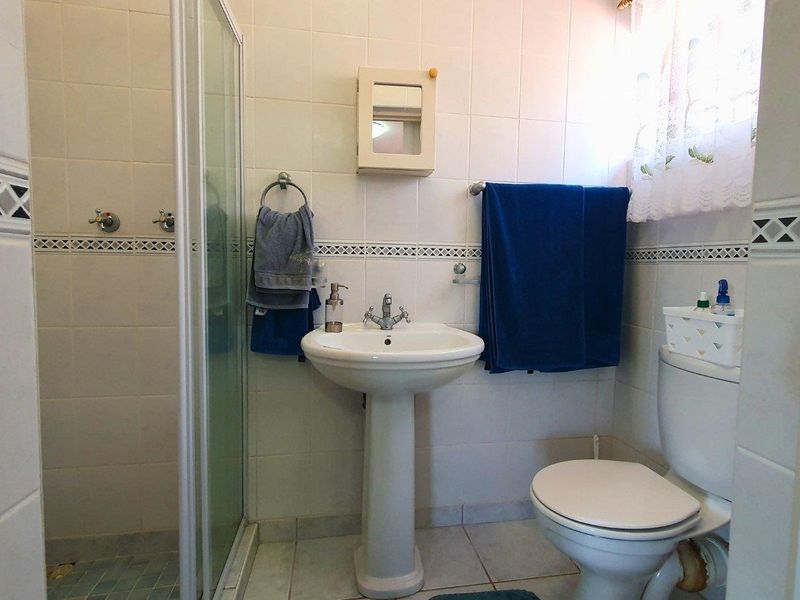A functional bathroom featuring a pedestal basin, a shower enclosure with glass doors, and a standard toilet, finished with classic ceramic wall and floor tiles.