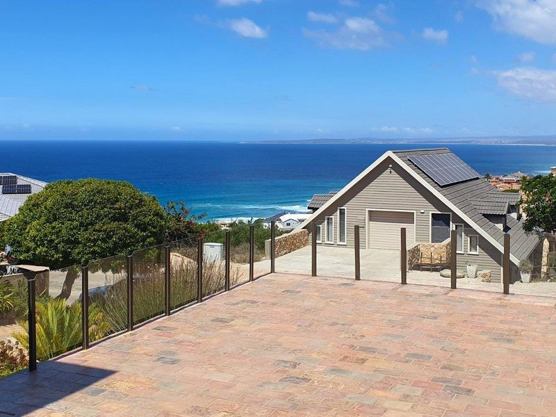 Spacious elevated patio featuring a glass balustrade, offering expansive ocean views and overlooking the adjacent property with solar panel installation.