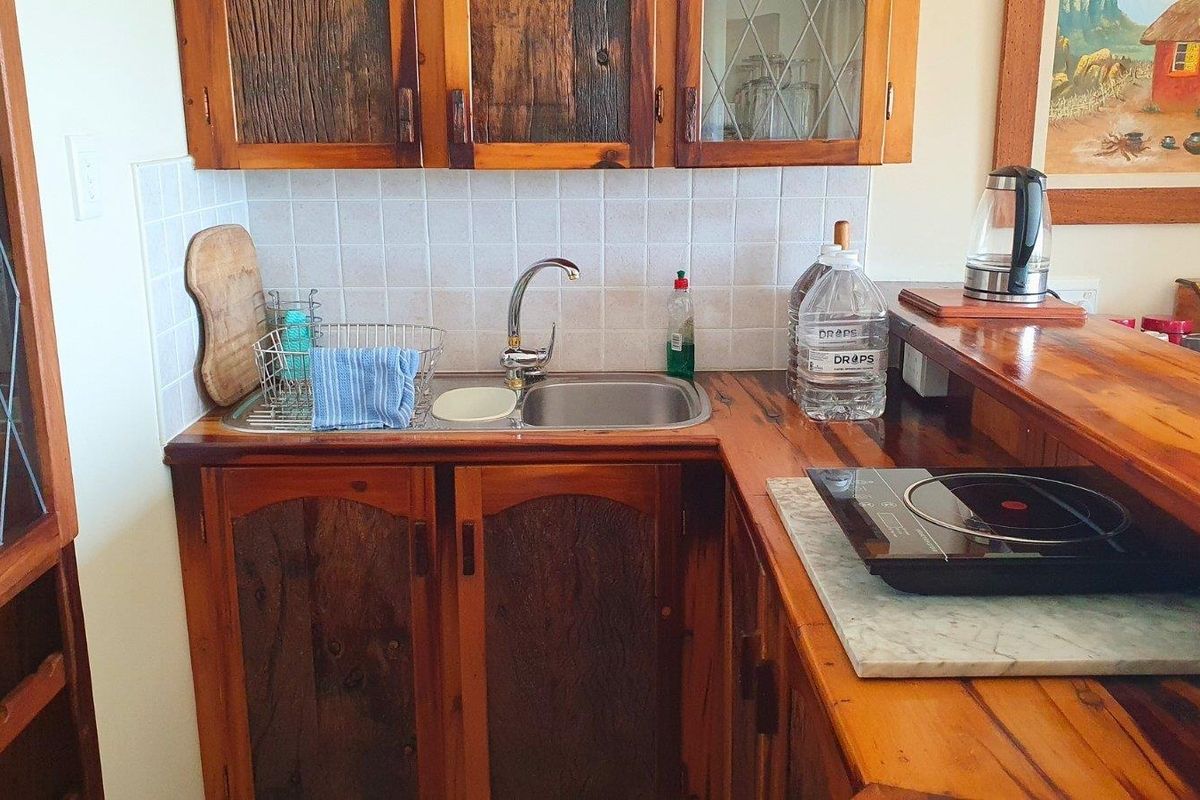 A compact kitchen area featuring rustic wooden cabinetry, a stainless steel sink, tiled backsplash, and a wooden breakfast bar counter.