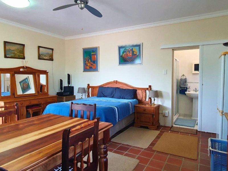 A bedroom featuring terracotta floor tiles, a ceiling fan, and an adjoining en-suite bathroom with a sliding door entrance.