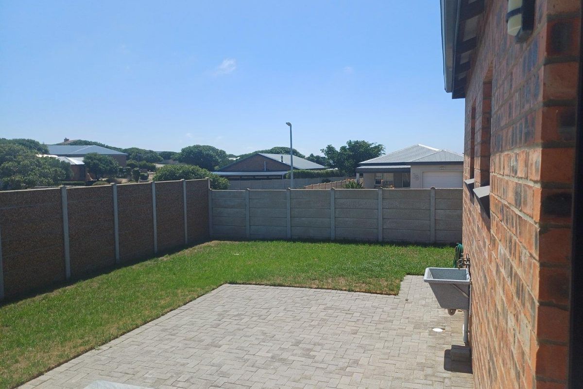 A private rear garden featuring a paved patio area, a small lawn, and perimeter precast concrete walling.