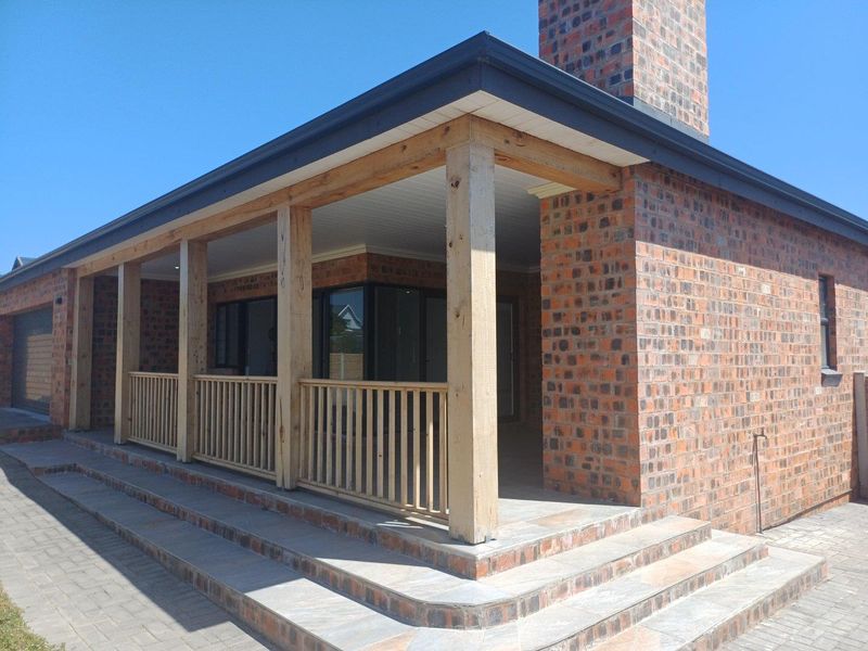 A covered patio area featuring exposed brickwork, timber support beams, a wooden balustrade, and tiled steps leading to the entrance.