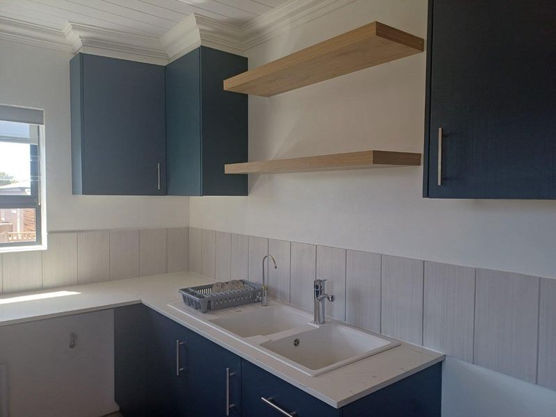 Modern kitchen scullery area featuring dark blue cabinetry, light stone countertops, a double basin sink, and floating timber shelves.