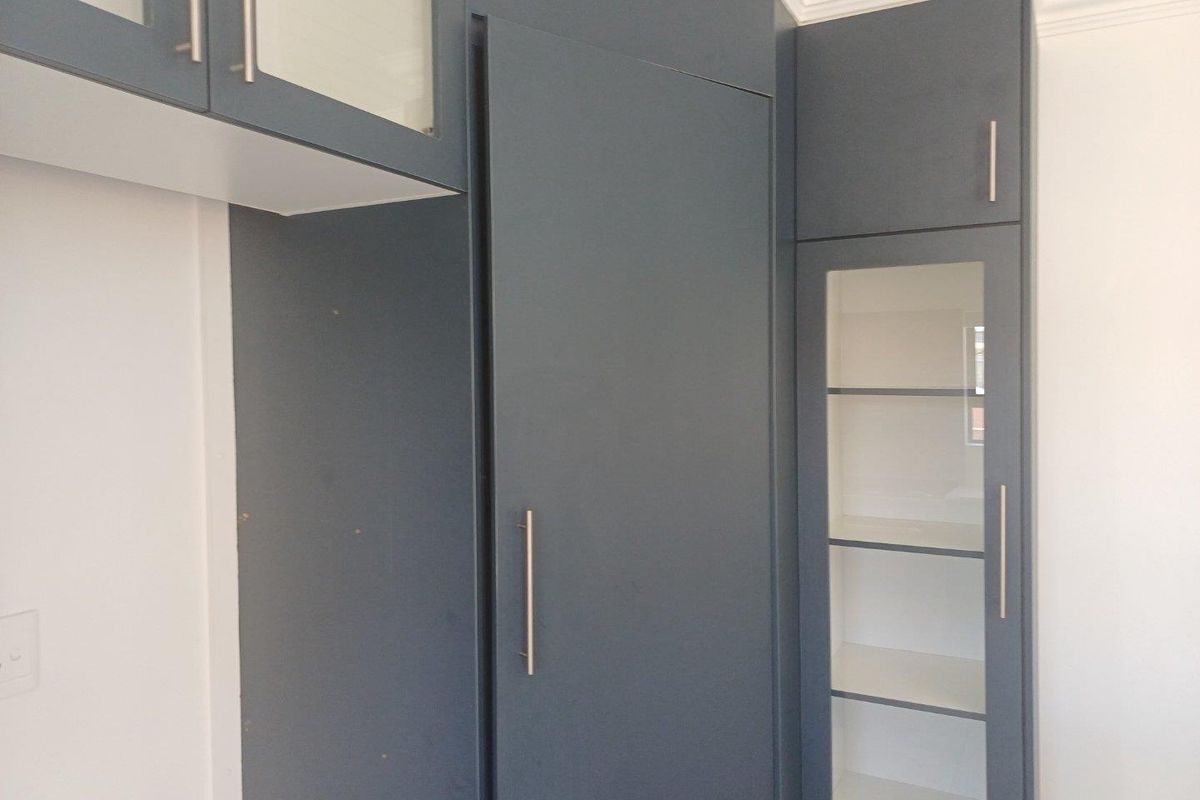 Modern dark grey built-in cabinetry featuring glass-fronted display shelving and sleek metal hardware, providing ample storage space.