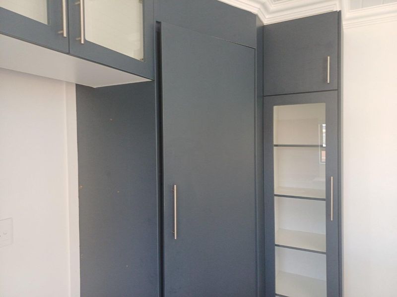 Modern dark grey built-in cabinetry featuring glass-fronted display shelving and sleek metal hardware, providing ample storage space.