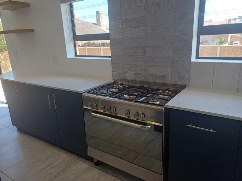 Modern kitchen featuring dark cabinetry, stone countertops, a stainless steel gas stove, and decorative tiled backsplash.