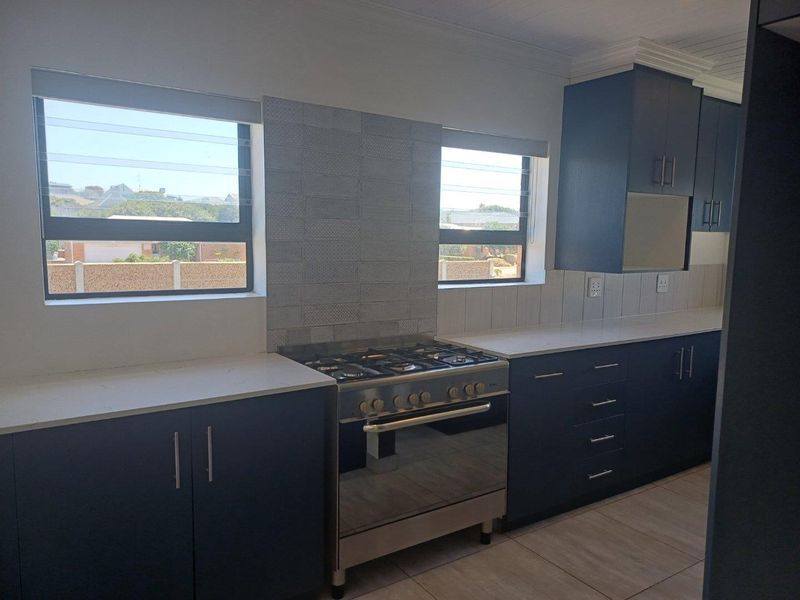 Modern kitchen featuring dark blue cabinetry, stone countertops, tiled backsplash, and a stainless steel gas stove with oven.