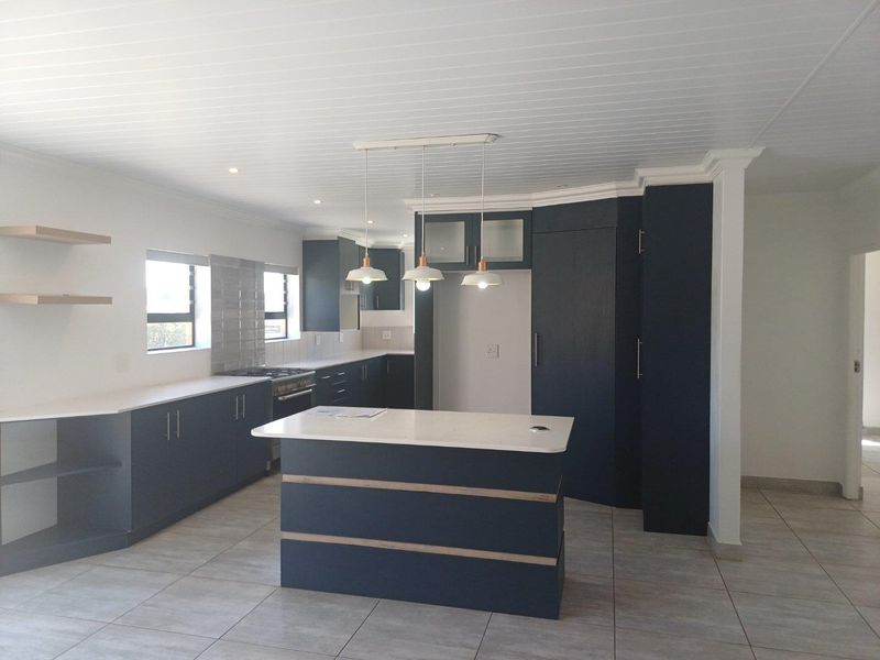 Modern kitchen featuring dark blue cabinetry, white stone countertops, a central island, and tiled flooring with integrated lighting.