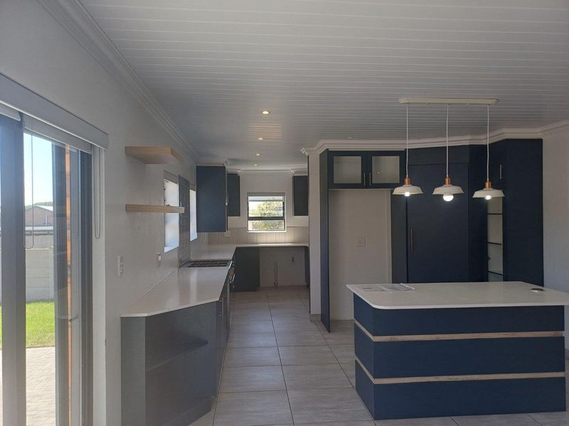 Modern kitchen featuring dark blue cabinetry, stone countertops, a central island, and integrated lighting, offering a clean and functional culinary space.