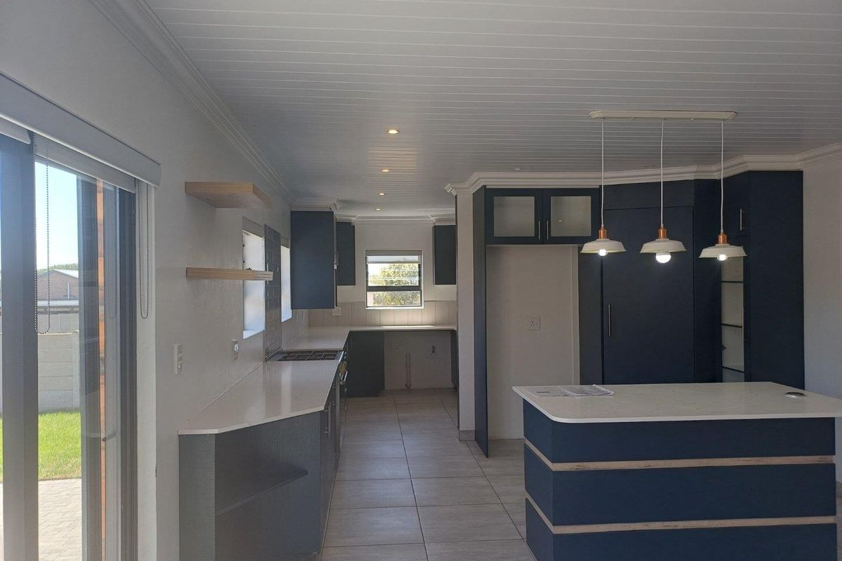 Modern kitchen featuring dark blue cabinetry, stone countertops, a central island, and integrated lighting, offering a clean and functional culinary space.