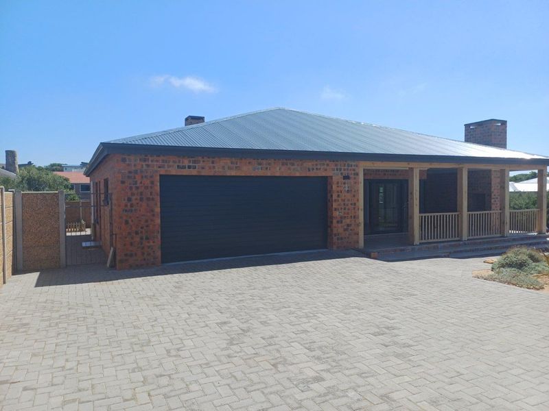 A well-maintained brick house featuring a double garage, a covered patio with wooden railings, and a paved driveway.