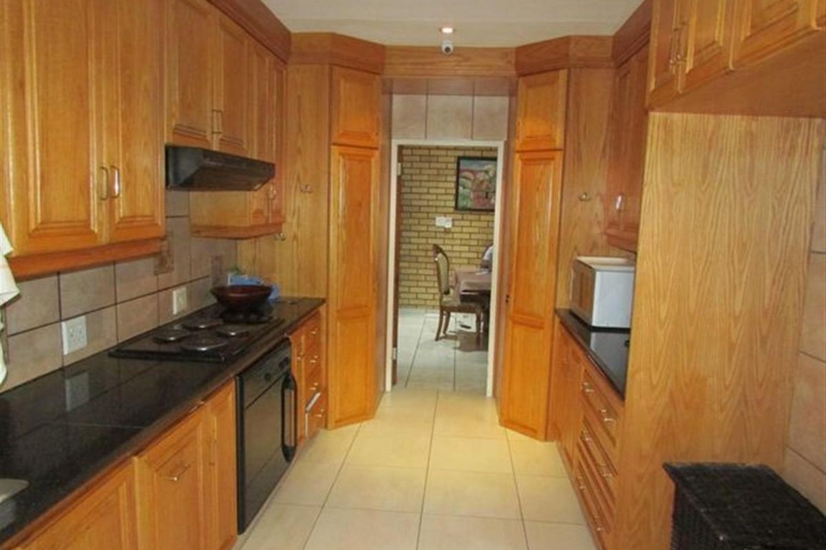 A functional kitchen featuring warm-toned wooden cabinetry, dark granite countertops, built-in appliances, and tiled flooring, leading through to an adjacent dining area.