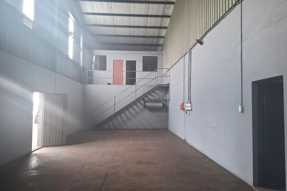 Spacious industrial warehouse unit featuring high ceilings, concrete flooring, a mezzanine level with staircase access, and multiple entry points.