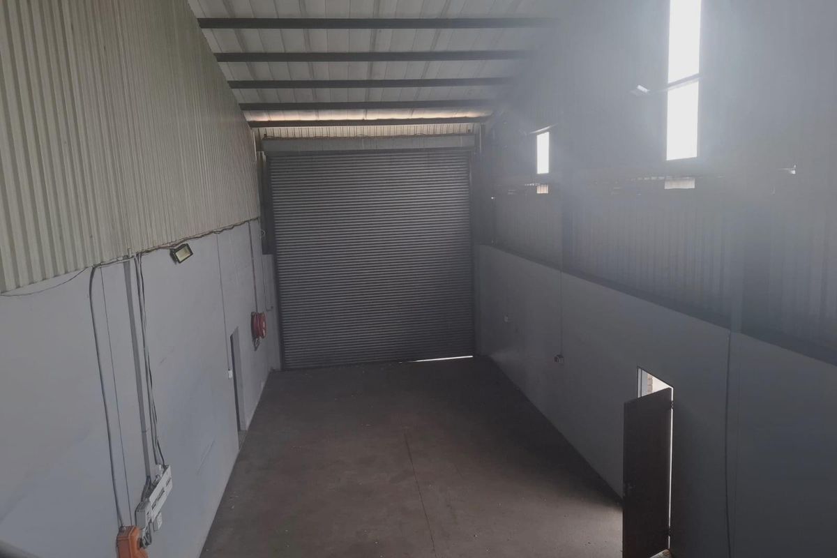 Spacious industrial warehouse unit featuring high ceilings, a large roller shutter door, concrete flooring, and integrated wall-mounted electrical fixtures.